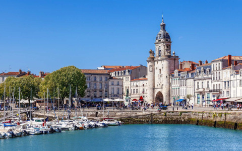 Barcos atracados en el puerto frente a edificios históricos y una torre del reloj en una ciudad costera francesa.