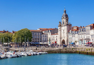 Boats docked in the harbor with historic buildings and a clock tower in a French coastal town on a sunny day.