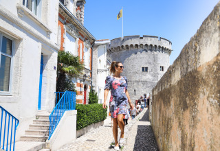 Donna che cammina su sentiero lastricato vicino a una torre storica a Flower Camping Tamarins Plage, Francia.