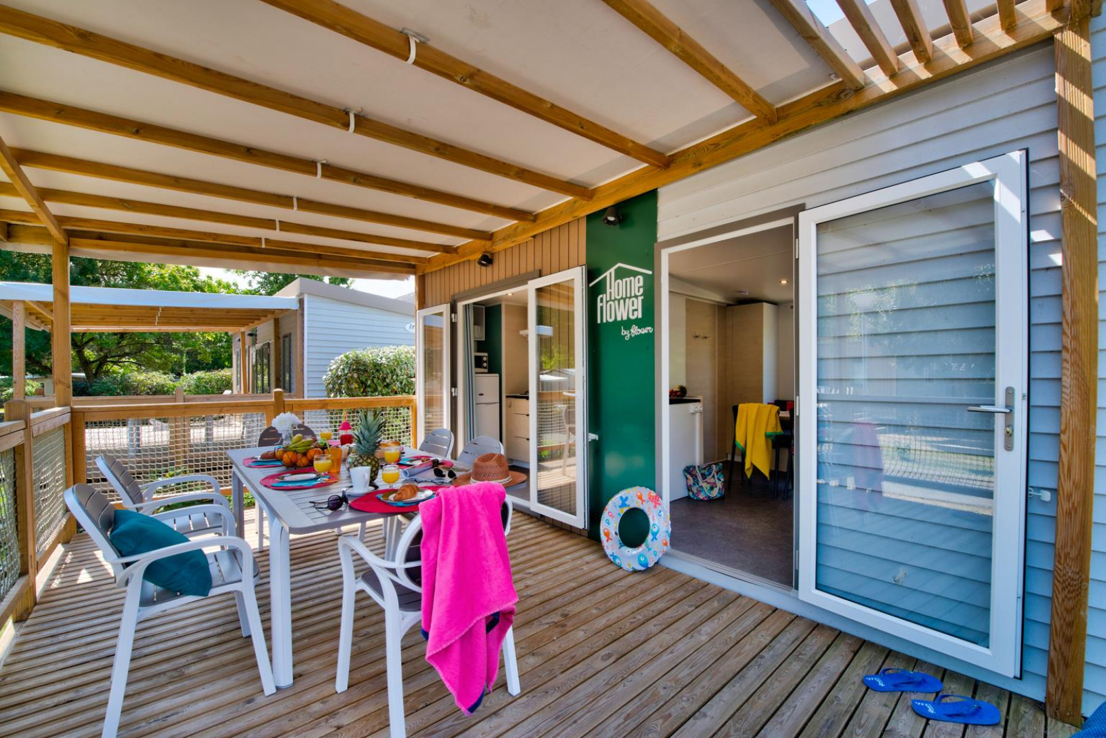 Overdekt terras bij glampingaccommodatie met gedekte ontbijttafel, stoelen en zomerse accessoires.