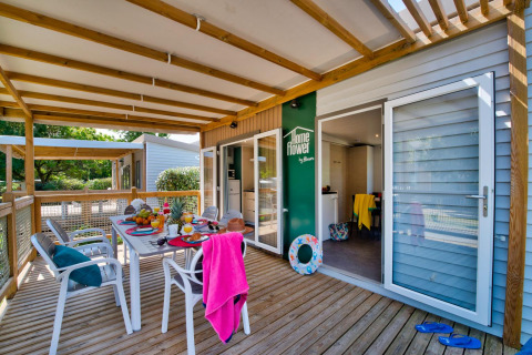 Terras met houten overkapping bij glampingverblijf, ontbijttafel gedekt en zomerse sfeer aanwezig.