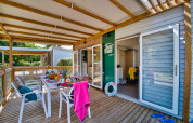 Überdachte Terrasse eines Glamping-Unterkunfts mit Frühstückstisch, Stühlen und sommerlicher Atmosphäre.