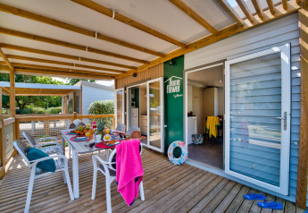 Überdachte Terrasse eines Glamping-Unterkunfts mit Frühstückstisch, Stühlen und sommerlicher Atmosphäre.