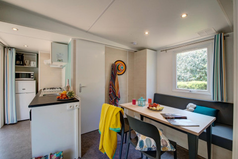 Modern glamping accommodation featuring a compact kitchen, dining table, large window, and cozy decor.