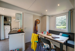 Moderne glampingaccommodatie met keuken, eettafel, groot raam en gezellige, kleurrijke inrichting.