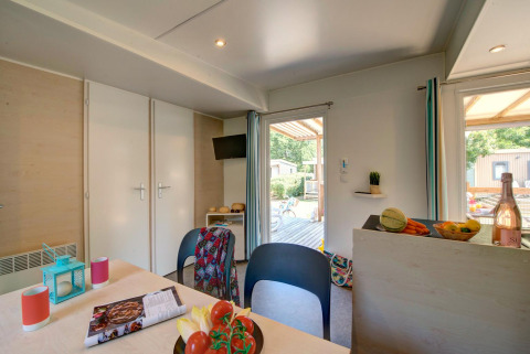 Binnenzicht van een glampingverblijf met eettafel, keukenhoek en toegang tot het terras buiten.