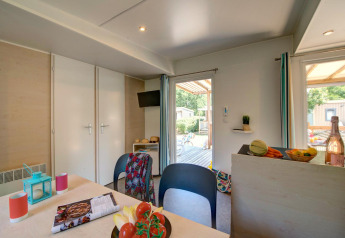 Vista interna di un alloggio glamping con tavolo da pranzo, cucina e accesso alla terrazza esterna.