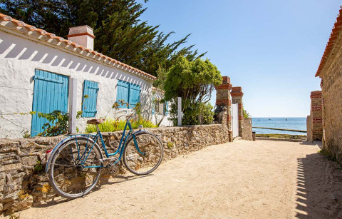 Bicicleta junto a un muro de piedra cerca de una casa blanca y azul, con vistas al mar en Tamarins Plage, Francia.
