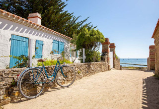 Fahrrad an einer Steinmauer vor einem weißen Haus mit blauen Fensterläden am Meer, Tamarins Plage, Frankreich.