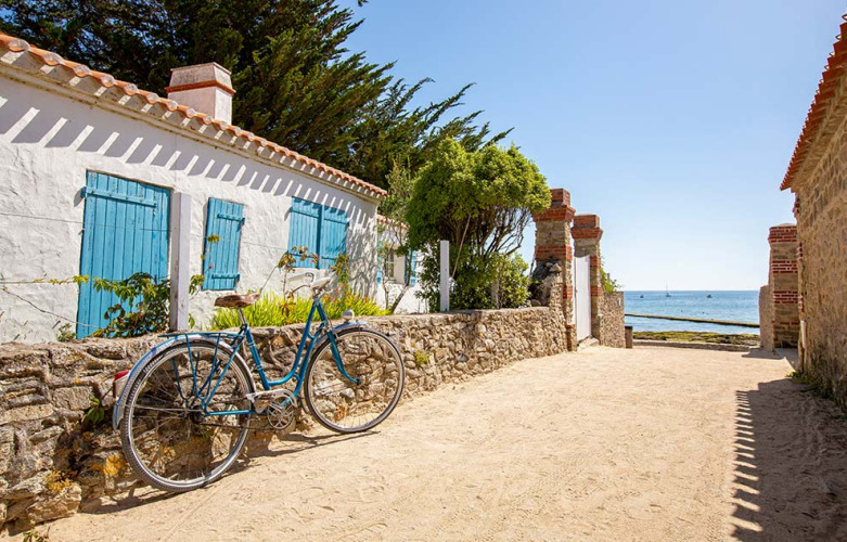 Cykel lænet op ad en stenmur ved en solrig sti nær havet på Flower Camping Tamarins Plage i Nouvelle-Aquitaine.