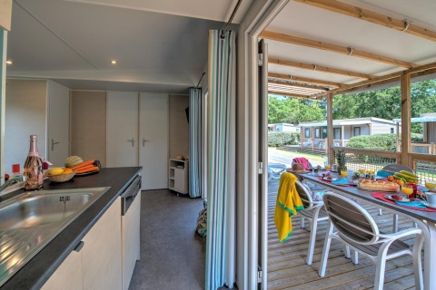 Lodgekeuken met verse groenten en fruit, kijkend uit op een terras met een gezellig gedekte eettafel buiten.