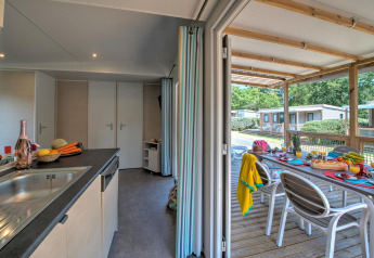 Et hyggeligt lodgekøkken med friske frugter og grøntsager, udsigt til en overdækket terrasse og udendørs bord.