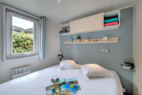 Modern glamping accommodation with a double bed, window, open shelves, and cozy decor in soft hues.
