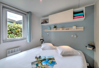 Moderne glampingaccommodatie met tweepersoonsbed, raam, open schappen en knusse, zachte inrichting.