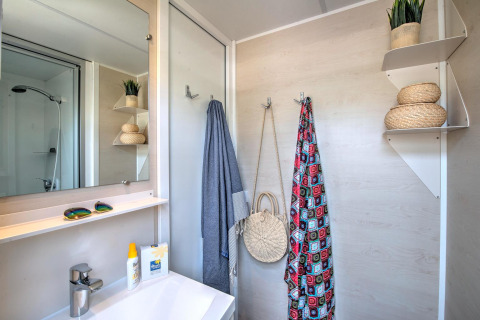 Modern bathroom in a glamping accommodation with sink, mirror, shower, and shelves with decorative baskets.