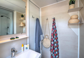 Moderne badkamer in een glampingverblijf met wastafel, spiegel, douche en decoratieve opbergmanden.