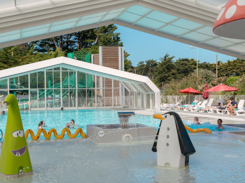Piscina coperta con scivoli d'acqua e giochi colorati al Flower Camping Le Bois d'Amour in Bretagna, Francia.