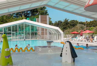 Piscina coperta con scivoli d'acqua e giochi colorati al Flower Camping Le Bois d'Amour in Bretagna, Francia.