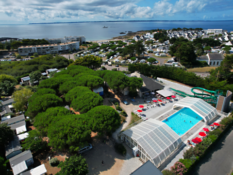 Aerial view of Flower Camping Le Bois d'Amour showing pools, lush trees, and coastline in Brittany, France.