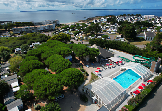 Aerial view of Flower Camping Le Bois d'Amour showing pools, lush trees, and coastline in Brittany, France.