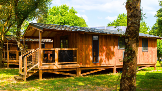 Chalet en bois au Lodge Premium VIP avec terrasse, entouré d’arbres et de verdure lors d’une journée ensoleillée.