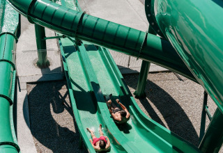 Two people slide down a green water slide at Flower Camping Le Bois d'Amour holiday park in Brittany, France.