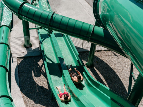 Deux personnes glissent sur un toboggan vert à Flower Camping Le Bois d’Amour, un parc de vacances en Bretagne, France.