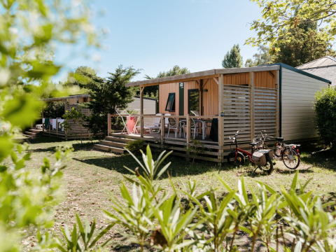 Cabañas de madera con porches y bicicletas fuera en Flower Camping Le Bois d'Amour, parque vacacional en Bretaña, Francia.