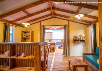 Interior view of a cozy glamping cabin featuring wooden furniture, open windows, and a covered patio.