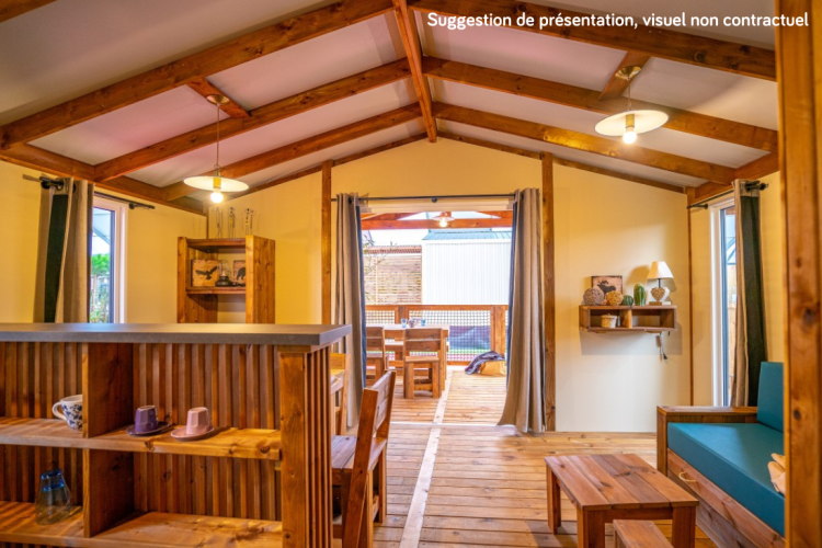 Vista interna di una accogliente sistemazione glamping con arredi in legno, finestre aperte e terrazza.