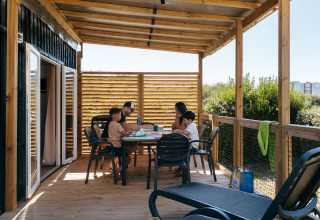 Family eating together on a covered wooden terrace at Flower Camping Le Bois d'Amour holiday park in Brittany, France.