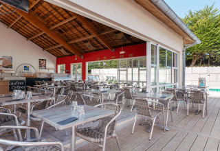 Zona de comedor al aire libre en Flower Camping Le Bois d'Amour, parque vacacional en Bretaña, Francia, junto a la piscina.