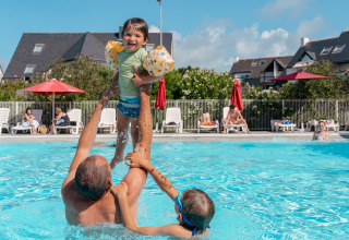 Un adulto gioca con due bambini in piscina al Flower Camping Le Bois d'Amour in Bretagna, Francia.