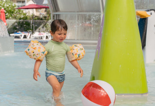 Bambino con braccioli gioca nell’acqua bassa di un villaggio turistico in Bretagna, Francia, vicino a un pallone.