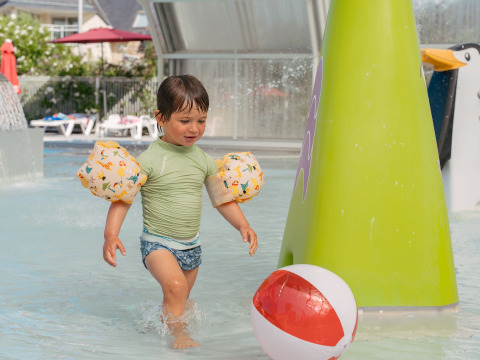 Young boy with floaties playing in shallow water at a holiday park in Brittany, France, near a beach ball.