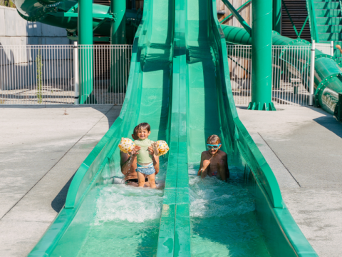 Two children playing on a green water slide at Flower Camping Le Bois d'Amour, Brittany, France.