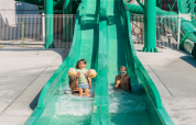Deux enfants s’amusent sur un toboggan aquatique vert à Flower Camping Le Bois d'Amour, Bretagne, France.