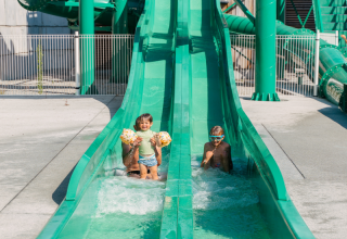 Two children playing on a green water slide at Flower Camping Le Bois d'Amour, Brittany, France.