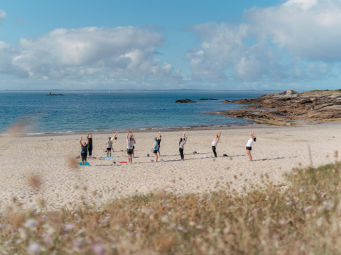 Grupo practicando yoga en la playa de Flower Camping Le Bois d'Amour, Bretaña, Francia, junto al mar.