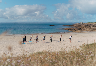 Gruppe beim Yoga am Strand im Flower Camping Le Bois d'Amour, Bretagne, Frankreich, mit Meerblick.