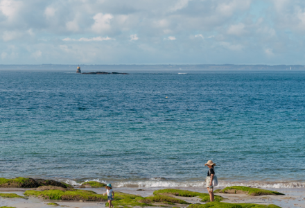 En mor og et barn nyder en dag på stranden nær Quiberon, Bretagne, med havet og en fyr i baggrunden.