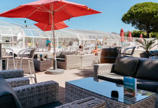 Outdoor lounge area at Flower Camping Le Bois d'Amour in Brittany, France, with pool, sofas, and red umbrellas.