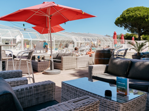 Outdoor lounge area at Flower Camping Le Bois d'Amour in Brittany, France, with pool, sofas, and red umbrellas.