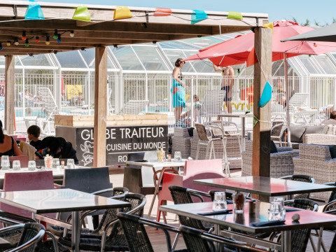 Terraza de restaurante al aire libre con vista a la piscina en Flower Camping Le Bois d'Amour, Bretaña, Francia.