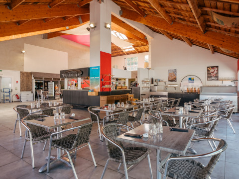 Indendørs restaurantområde på Flower Camping Le Bois d'Amour feriepark i Bretagne, Frankrig, med tomme borde.