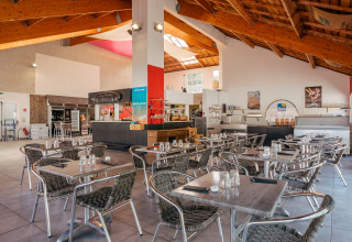 Zona de comedor interior en Flower Camping Le Bois d'Amour, parque vacacional en Bretaña, Francia, con mesas vacías.