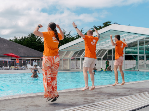 Tres personas saltan juntas a la piscina en Flower Camping Le Bois d'Amour, un parque vacacional en Bretaña, Francia.