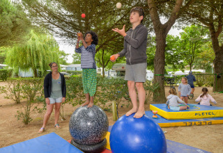 Niños haciendo malabares sobre pelotas grandes en Flower Camping Le Bois d'Amour en Bretaña, Francia.