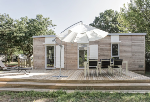 Lodge in legno con terrazza, ombrellone e tavolo da pranzo al Flower Camping L'Ile d'Offard, Francia.