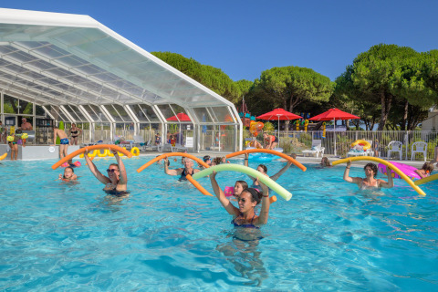 Vakantiegangers nemen deel aan aquagym met schuimslangen in het zwembad van Flower Camping Le Bois d’Amour, Bretagne.